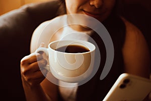 Woman's hand holding a phone and a cup of coffee. Technology and home concept.