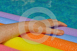 Woman\'s hand holding rainbow pool noodles in swimming pool