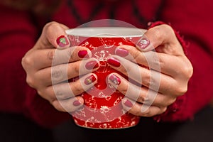 Woman`s hand holding a red cup of coffee. With a beautiful winter manicure.