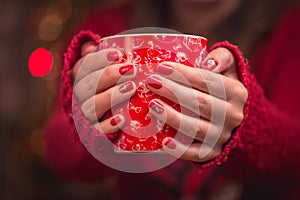 Woman`s hand holding a red cup of coffee. With a beautiful winter manicure.