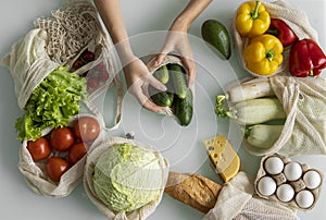 Woman`s hand, holding a reusable grocery bag with vegetables on a kitchen at home and takes cucumber out. Zero waste and