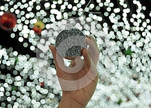 Woman`s hand holding silver chritmas ball with bokeh light backdrop.