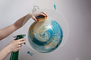 Woman& x27;s hand holding a sponge and spray to clear the planet Earth. Concept of improving the state of the environment