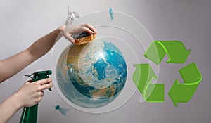 Woman`s hand holding a sponge and spray to clear the planet Earth. The sign of recycle. The concept of improving the state of the
