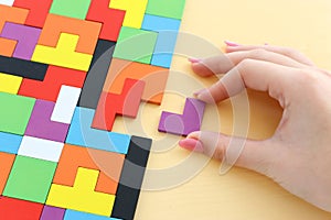 Woman`s hand holding a square tangram puzzle, over pastel wooden table