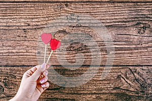 Woman`s hand holding two red hearts shape on stick. Dark wooden baskground. Valentine concept.