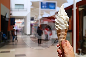 Woman`s hand holding vanilla milk soft serve ice cream cone in the sunlight