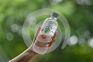 A woman`s hand is holding a water bottle with a black lid, a green background