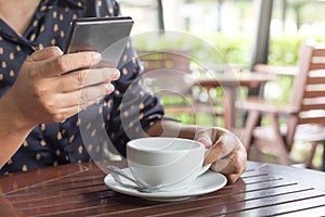 Woman`s hand holding a white coffee cup and smartphone in cafe blurred background  with morning sunlight