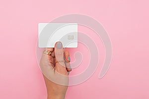 Woman`s hand holding white credit or debit card with chip over the pink background