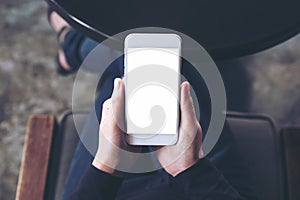 A woman`s hand holding white mobile phone with blank desktop screen on thigh in cafe