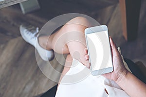 Woman`s hand holding white mobile phone with blank screen on thigh with wooden floor background in modern