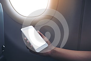 Woman`s hand holding a white smart phone with blank desktop screen next to an airplane