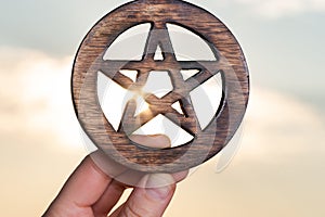 Woman`s hand holding Wooden encircled Pentagram symbol at sunrise in front of the lake. Concept of Five elements