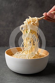 Woman`s hand holds bamboo sticks with noodles in a white bowl bowl on a dark slate stone background