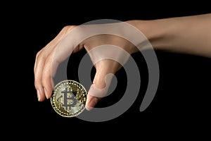 Woman& x27;s hand holds a bitcoin in her fingers. Isolated on black background