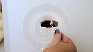 A woman's hand holds a burning match to set fire to a gas boiler.