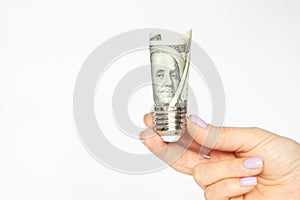 A woman& x27;s hand holds a cartridge from a light bulb with dollars on a white background, the price of electricity