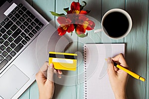 Woman`s hand holds credit card over table, online shopping gifts through phone during coffee break