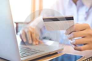 A woman`s hand holds a credit card and uses a laptop to shop onl