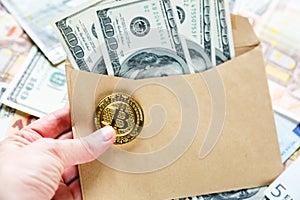 Woman`s hand holds an envelope with dollars and bitcoin. Investment, risk, salary, savings