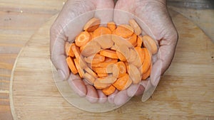 A woman's hand holds a fresh and clean cut carrot, wooden cutting board background,