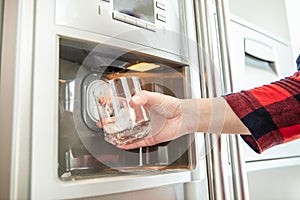 Woman`s hand holds glass and uses refrigerator photo