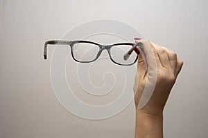 A woman`s hand holds glasses, selection of glasses to improve vision on a gray background, recommendations of ophthalmologists