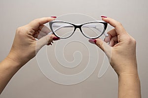 A woman`s hand holds glasses, selection of glasses to improve vision on a gray background, recommendations of ophthalmologists