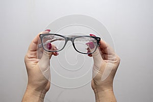 A woman`s hand holds glasses, selection of glasses to improve vision on a gray background, recommendations of ophthalmologists