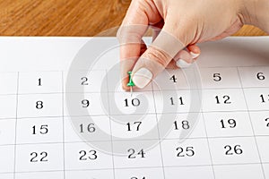 A female hand with a beautiful manicure holds a green pushpin to mark the date on the calendar 10 day
