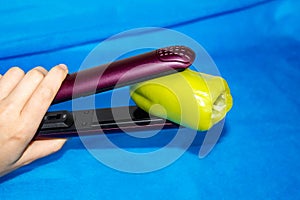 A woman`s hand holds a hair Styler green bell pepper on a blue background