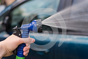 A woman`s hand holds a hose for washing the car. Water, spray, jet. The idea is to wash your car in front of your house