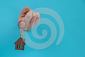A woman's hand holds the keys with a keychain in the shape of a house on a blue background.