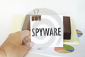 Woman s hand holds a piece of paper with text spyware on the background of graphs and notepad