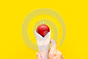 Woman`s hand holds red Christmas ball in waffle cone over bright yellow background. Mnimal concept, top view. Xmas or New Year gre
