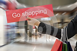 woman's hand holds shopping bags and a sign that says go shopping. The concept of shopping and shopaholism photo