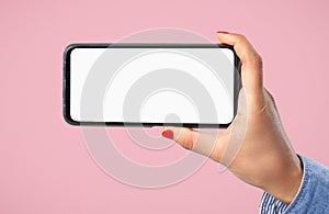 A woman`s hand holds a smartphone with a blank white screen horizontally. On a pink background