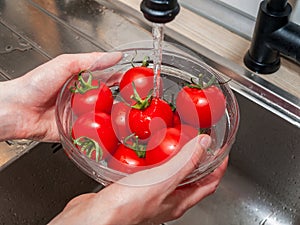 a woman`s hand holds tomatoes under running tap water, the importance of handling and thoroughly washing vegetables and fruits du