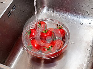 A woman`s hand holds tomatoes under running tap water, the importance of handling and thoroughly washing vegetables and fruits du