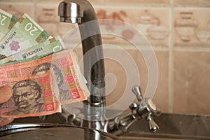 Woman`s hand holds a Ukrainian 10 20 hryvnia near the kitchen tap, water prices