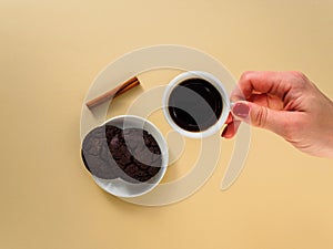 A woman`s hand holds a white Cup of black coffee. Chocolate chip cookies and cinnamon