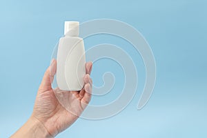 Woman`s hand holds white plastic tube on blue background. Ð¡osmetic bottles for beauty or medicine products