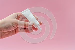 Woman`s hand holds white plastic tube on pink background. Ð¡osmetic bottles for beauty or medicine products