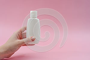 Woman`s hand holds white plastic tubes on pink background. Ð¡osmetic bottles for beauty or medicine products