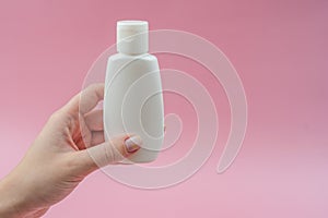 Woman`s hand holds white plastic tubes on pink background. Ð¡osmetic bottles for beauty or medicine products