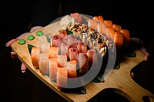 Woman's hand holds wooden board with Philadelphia Sushi roll set with salmon, tuna, and eel