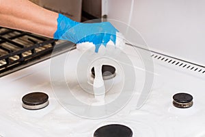 Woman`s hand in a household glove washing sponge with foam a gas stove and burners on the kitchen, close up