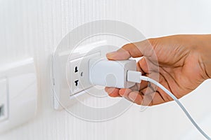 Woman`s Hand Inserting Electrical Power Cord Plug into Receptacle on wall outlet