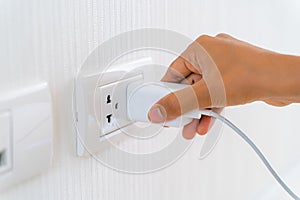 Woman`s Hand Inserting Electrical Power Cord Plug into Receptacle on wall outlet